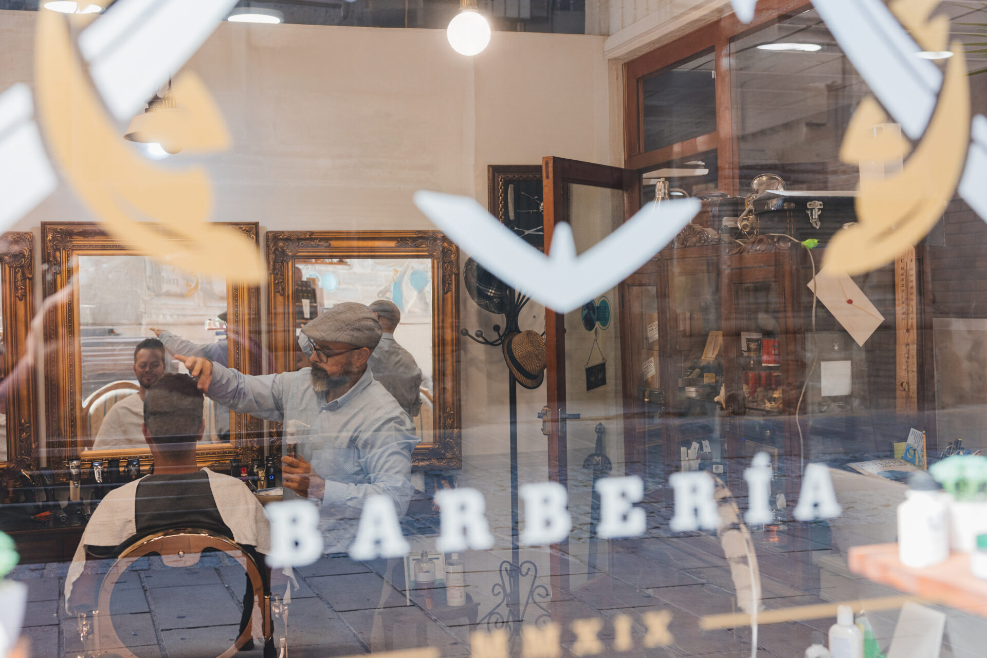 Foto desde fuera de la barberia desde donde se ve el interior mientras un barbero trabaja