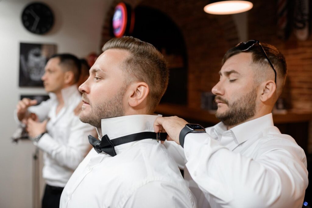 Vista lateral novio confiado barba bigotes pie mirando otro lado mientras su amigo esta detras el lo ayuda vestirse camisa corbata mono habitacion hotel dia boda 8353 12417