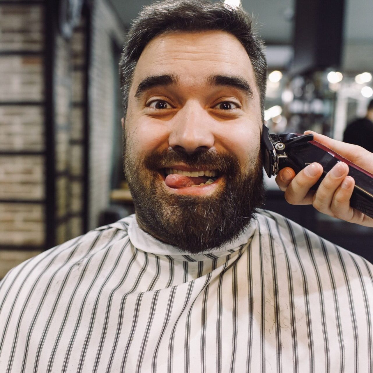 Cliente sacando la lengua de forma graciosa mientras que barbero trabaja el peluquería